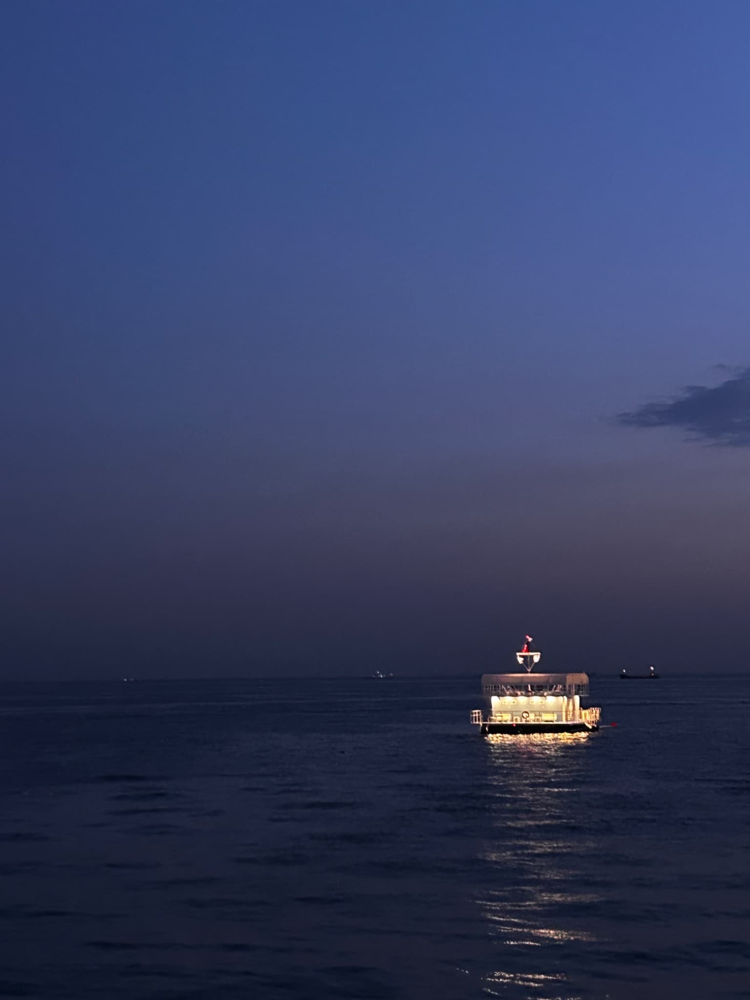 A single lit boat moves across open water at dusk.